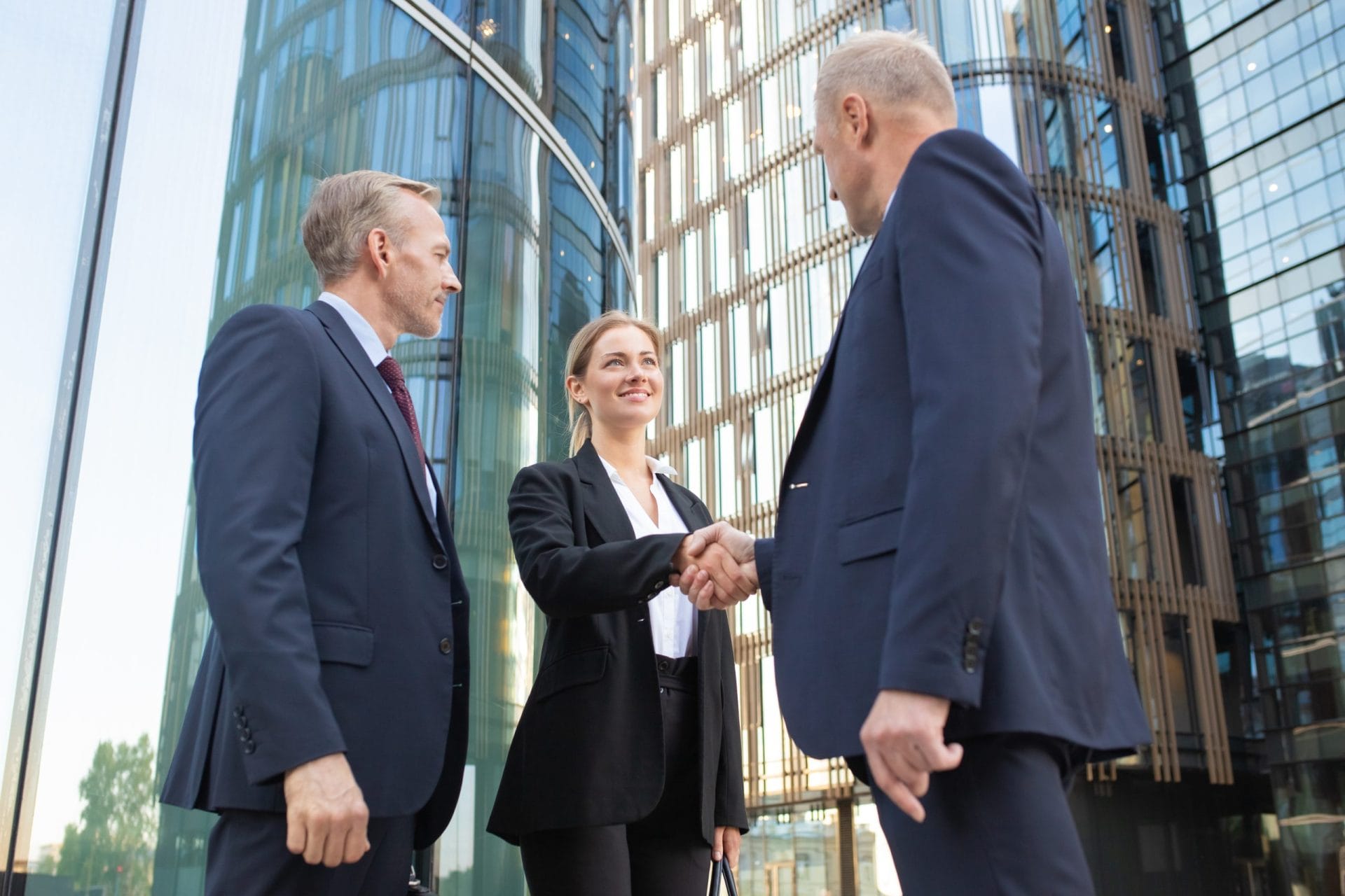 M&A process shown as a group of people shake hands symbolizing a business deal which is happening in front of tall buildings