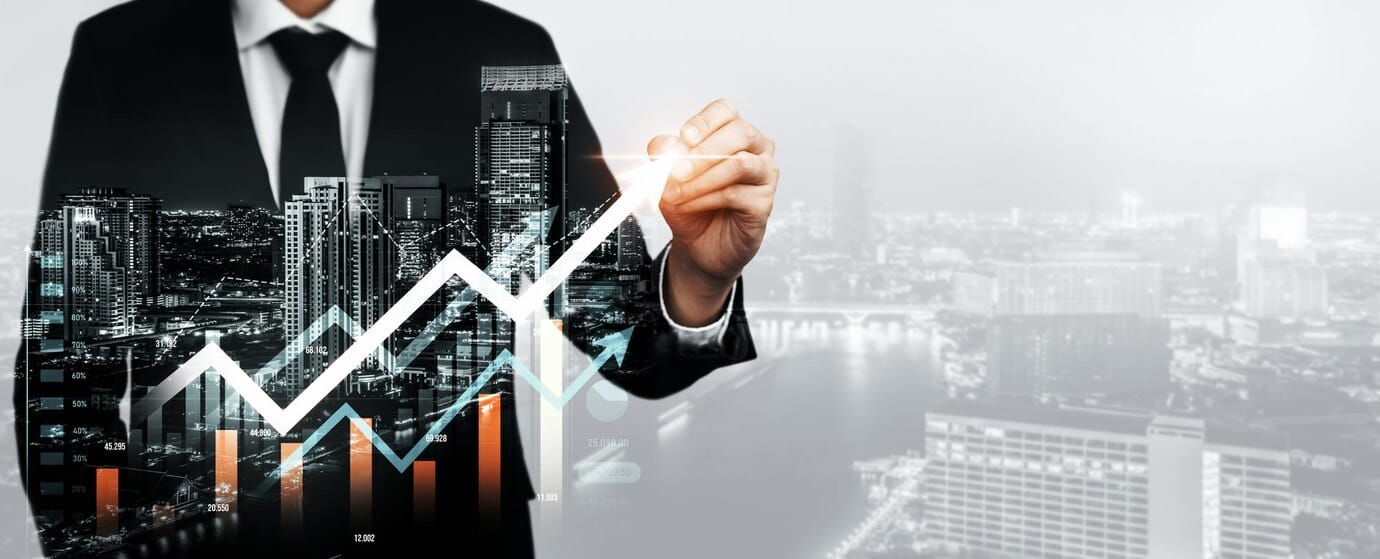 Čovek u odelu crta grafikon koji prikazuje finansijske performanse ili ekonomski rast, na transparentnom ekranu ili staklu. U pozadini je panorama grada, koja simbolizuje javni poziv za ulaganja u Bosni i Hercegovini.