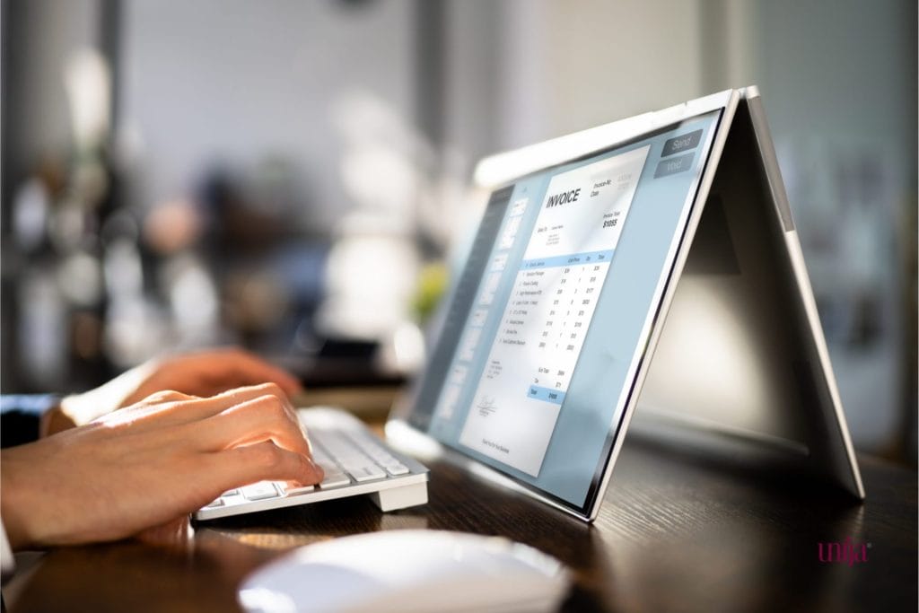 Ruke kucaju na tastaturi modernog laptopa, na čijem je ekranu otvorena e-faktura koja prikazuje različite stavke sa cenama i ukupnim iznosom, što simbolizuje izmene i dopune Pravilnika koje se odnose na interni račun za promet stranog lica u Srbiji.