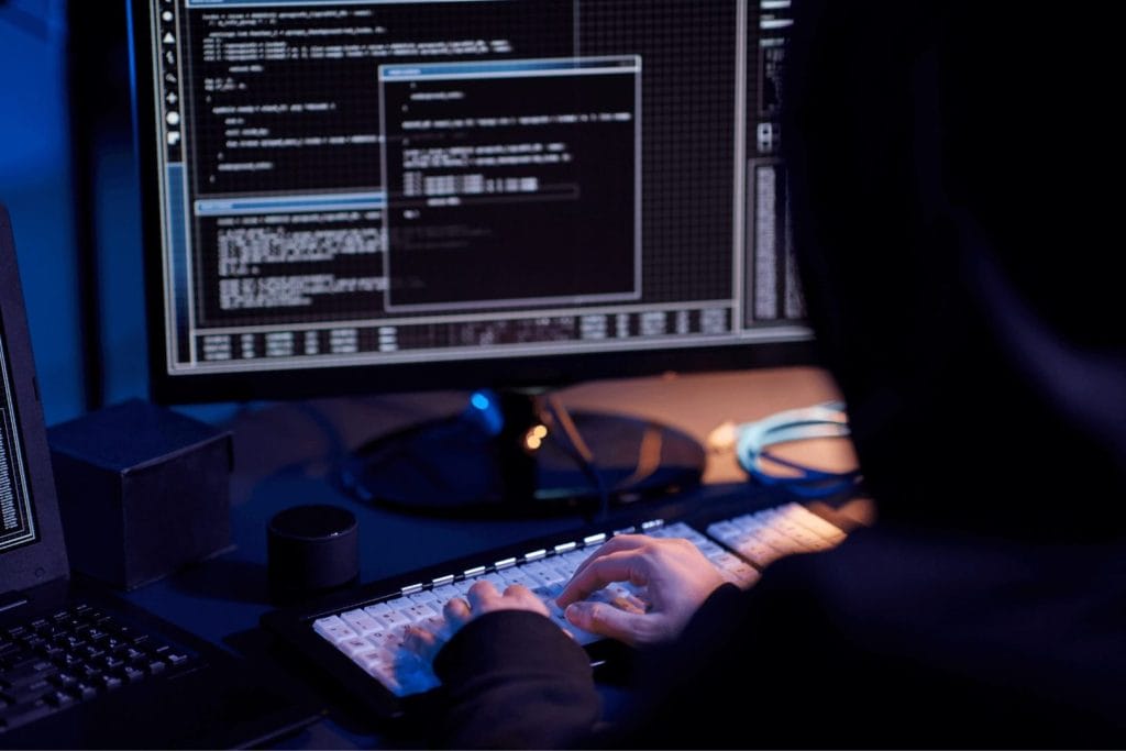 Osoba radi na računaru u okruženju fokusiranom na IT sigurnost, dok na ekranima prikazuje mrežne podatke i aktivnosti povezane sa cyber prijetnjama poput DDoS napada. 