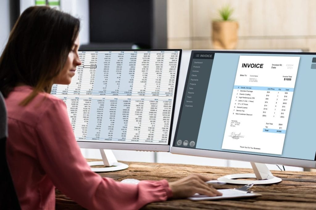 Računovodstveni servis u Hrvatskoj – računovođa radi na dva monitora, analizirajući financijske podatke i fakture, što simbolizira digitalizirano računovodstvo i učinkovito upravljanje dokumentima.