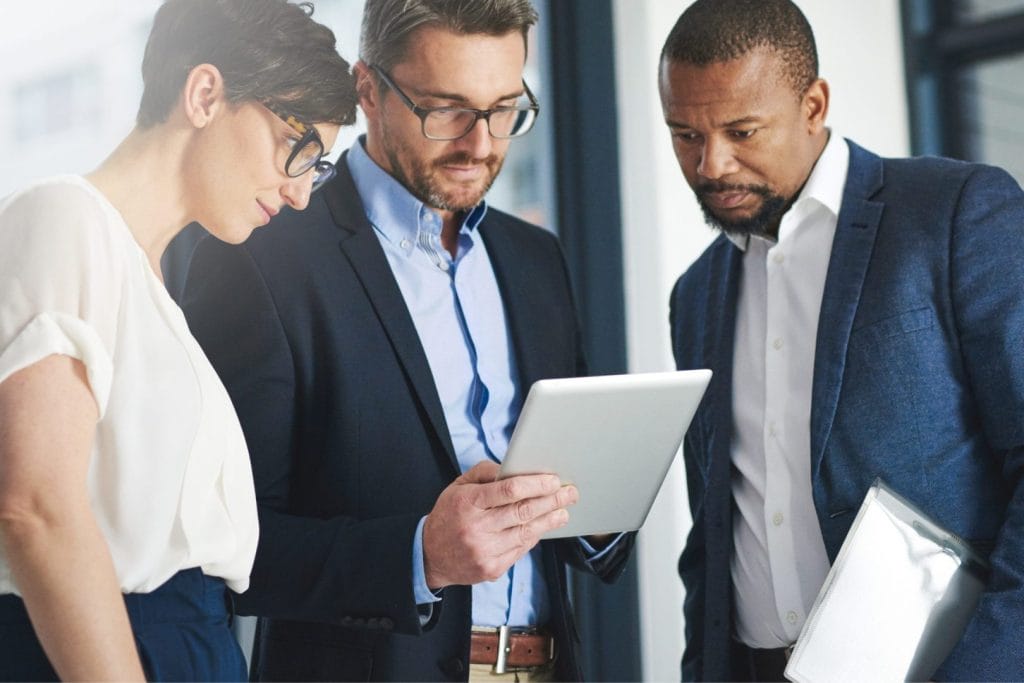 Biznismeni i investitori u poslovnoj diskusiji analiziraju podatke na tabletu. Fokusirani su na strateško planiranje i donošenje odluka o budućim investicijama.)