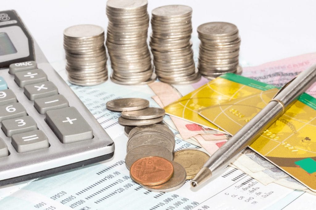 Kalkulator, gomile novčića, papirne novčanice, kreditne kartice i hemijska stoje preko finansijskih dokumenata. Ilustracijom se simbolizuju podsticaji za MSP u Srbiji.