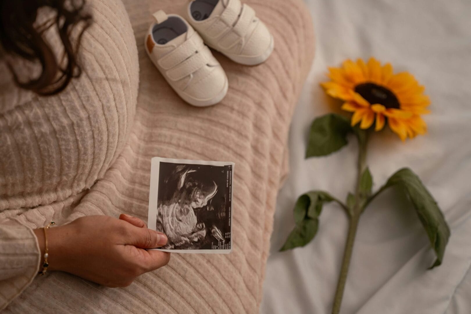 Trudnica sa ultrazvučnim snimkom drži cipele i suncokret, simbolizuje porodiljsko bolovanje u Srbiji.